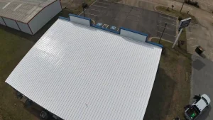 Aerial drone view of a bright white reflective roof coating on a commercial metal building with blue trim.