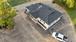 class 3 vs class 4 shingles A high-angle drone photograph captures a clean-looking commercial property with an immaculate black asphalt shingle roof, emphasizing its condition as if protected by a comprehensive roof maintenance plan, featuring detailed roofline vents, fascia, and surrounding parking area with a white pickup truck.